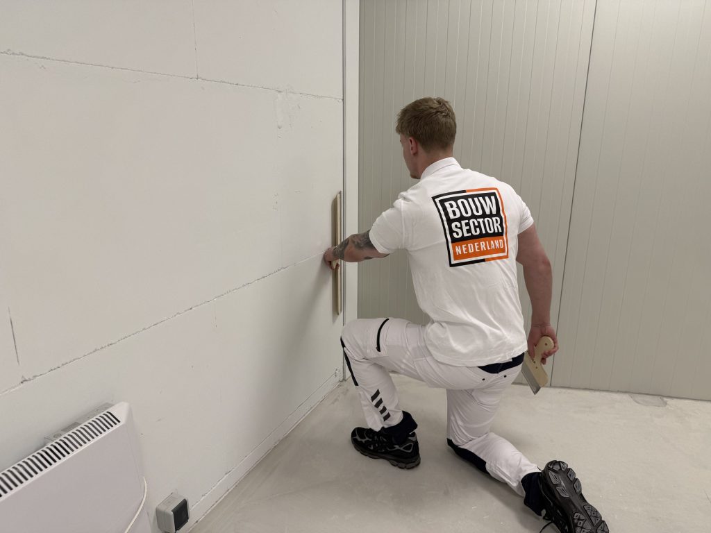 Stukadoor zit op een knie en trekt het onderste deel van een binnenwand vlak met een spaan