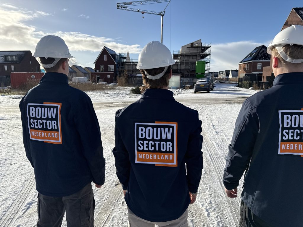 Medewerkers van Bouwsector Nederland met helm en werkjas bij een nieuwbouwproject met een bouwkraan